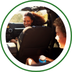 A mother turns from the front passenger seat of a vehicle to smile at her young child.